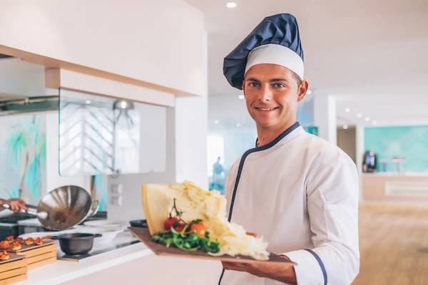 Ein Koch im Iberostar Waves Alcudia Park Hotel präsentiert ein Gericht in der Küche.