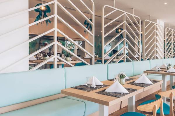 Innenbereich des Iberostar Waves Alcudia Park Hotels mit hellblauen Sofas, Holztischen und geometrischen Wanddesigns.