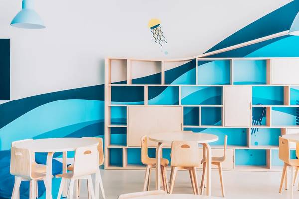 Kinderzimmer im Iberostar Waves Alcudia Park mit blauen und weißen Wänden, einem Bücherregal, und runden Tischen und Stühlen.