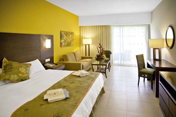 Ein luxuriöses Zimmer im Dreams Royal Beach Punta Cana mit gelben Wänden, einem großen Bett, einem Sofa und einem Tisch mit Blumen.