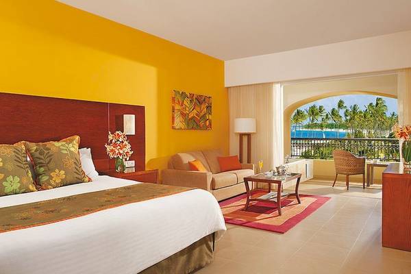 Suite-Zimmer im Dreams Royal Beach Punta Cana mit gelben Wänden, einem Bett, einem Sofa, einem Tisch und einem Balkon mit Meerblick.