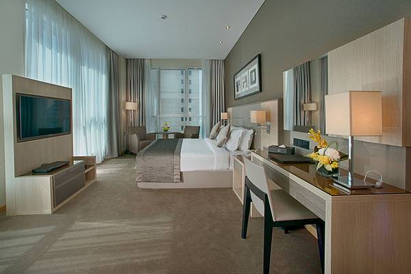 Innenansicht eines Hotelzimmers im TRYP by Wyndham Abu Dhabi City Center mit Bett, Fernseher, Schreibtisch und Stühle.