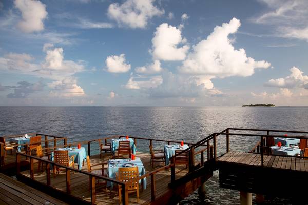 Außenterrasse des Coco Bodu Hithi Hotels mit Blick auf das Meer und blaue Tische.