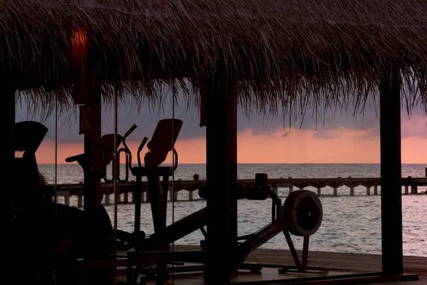 Fitnessstudio im Coco Bodu Hithi Hotel mit Blick auf den Sonnenuntergang am Meer.