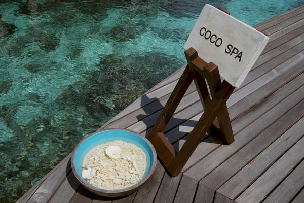 Ein Schild mit der Aufschrift Coco Spa neben einer Schale mit Sand und Muscheln am Wasser.