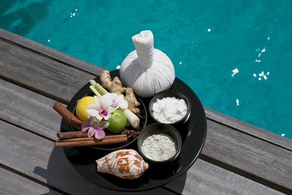 Eine Schale mit Spa-Zutaten vor einem Pool, einschließlich Ingwer, Zitronen, Gewürzen, Salz und einer Blume.