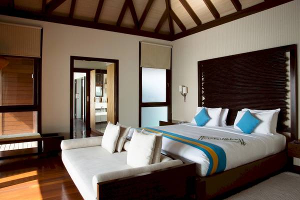 Schlafzimmer im Coco Bodu Hithi Hotel mit Doppelbett, Kissen und Fenstern.