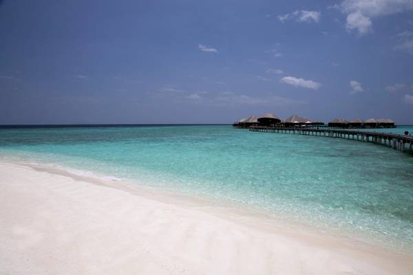 Strand des Coco Bodu Hithi Hotels mit weißen Sand und Wasservillen im Hintergrund