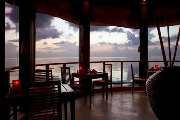 Abendliche Aussicht vom Coco Bodu Hithi Restaurant auf das Meer mit stimmungsvollen Kerzen und Möbeln.