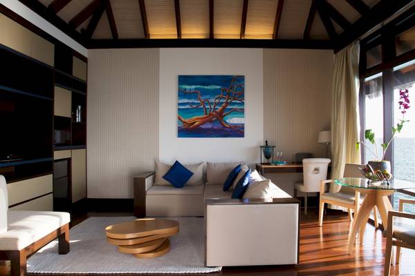 Innenansicht des Wohnzimmers im Coco Bodu Hithi Hotel mit Sofa, Tisch und Meeresblick.