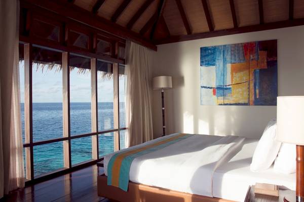 Schlafzimmer im Coco Bodu Hithi Hotel mit Blick auf das Meer von einem großen Fenster aus.