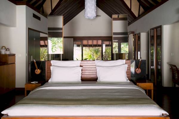 Schlafzimmer im Coco Bodu Hithi Hotel mit großem Bett und weißen Kissen vor einem Fenster.