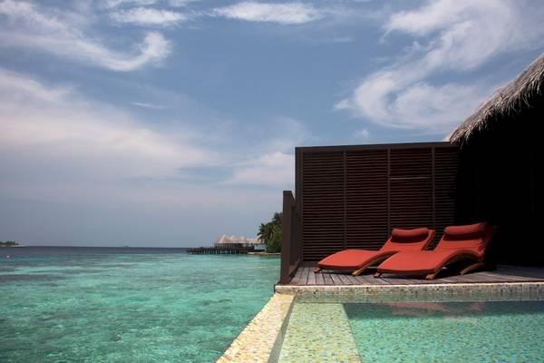 Rote Loungesessel auf dem Pooldeck des Coco Bodu Hithi Hotels mit Blick auf das Meer.
