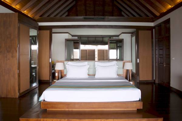 Schlafzimmer im Coco Bodu Hithi Hotel mit Bett, Lampen und Holzelementen.