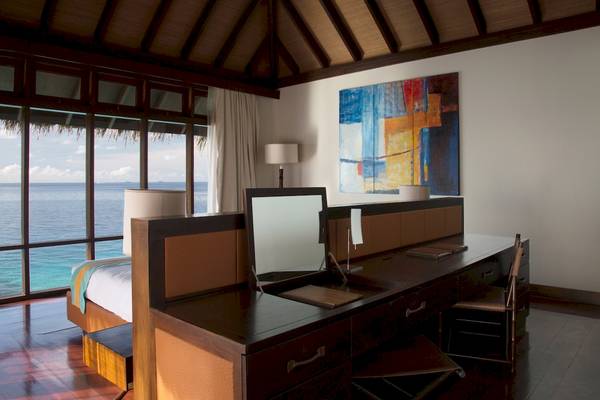Innenansicht eines Coco Bodu Hithi Hotelzimmers mit Schreibtisch, Stuhl, Bett und Meerblick.