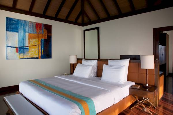 Schlafzimmer im Coco Bodu Hithi Hotel mit einem großen Bett, weißen Kissen und einer modernen Wandkunst.