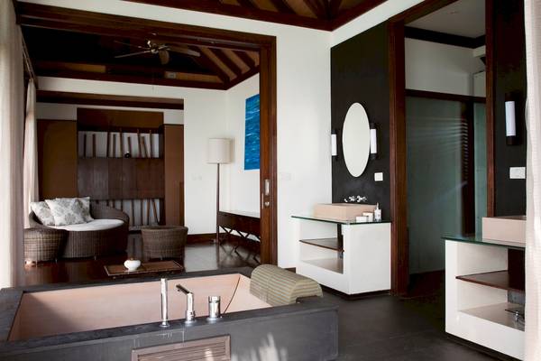 Innenansicht des Badezimmers im Coco Bodu Hithi Hotel mit Badewanne, Spiegel und Möbeln.