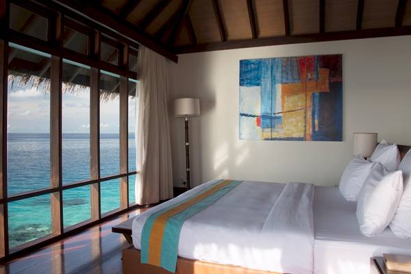 Schlafzimmer im Coco Bodu Hithi Hotel mit Blick auf das Meer durch große Fenster.