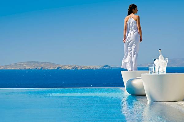 Frau in weissem Kleid am Pool des Mykonos Grand Hotel mit Blick auf das Meer