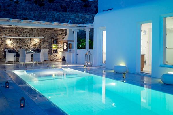 Nachtansicht des Swimmingpools im Mykonos Grand Hotel & Resort mit blauem Licht und steinerner Wand.