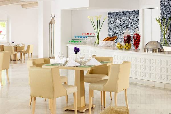Restaurant des Mykonos Grand Hotel & Resort mit modernem Design, Tischen und Stühlen, einer Bar und dekorativen Elementen.