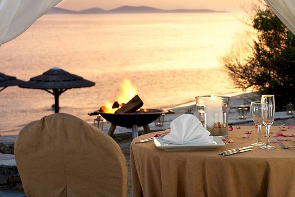 Abendessen am Strand im Mykonos Grand Hotel & Resort mit Blick auf den Sonnenuntergang und einem offenen Feuer.