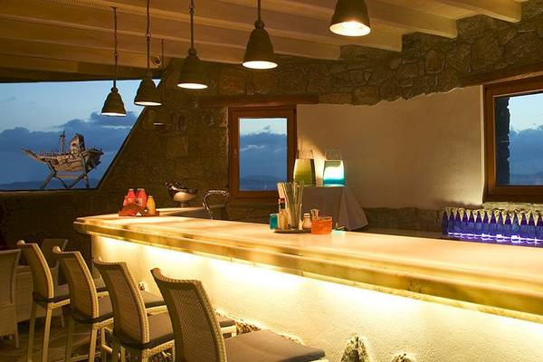 Innenansicht der Bar im Mykonos Grand Hotel & Resort mit einer Theke, Stühlen und dekorativen Flaschen.