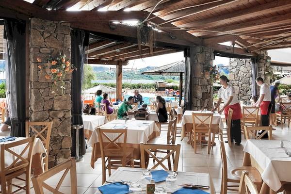 Innenansicht des Restaurants im Resort Cala Di Falco mit Gästen an Tischen und Blick auf den Pool.