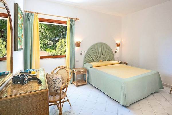 Doppelzimmer im Resort Cala Di Falco mit Bett, Nachttischen, Stühlen und Fenstern.