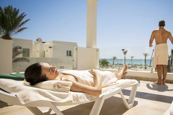 Eine Frau entspannt sich auf einem Liegestuhl auf dem Balkon des Robinson Djerba Bahiya Hotels mit Blick auf das Meer.