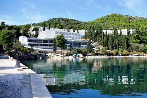 Außenansicht des Osmine Slano Hotels am Wasser mit grünen Bäumen und Gebäuden im Hintergrund.