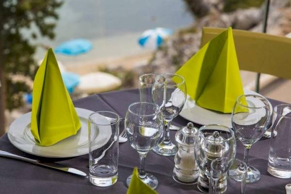 Ein Tisch auf der Terrasse des Osmine Slano Hotels mit grünen Servietten und Gläsern.