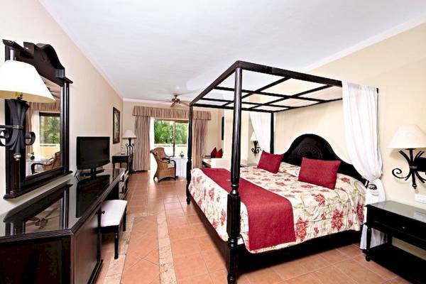 Hotelzimmer mit Baldachin-Bett, Dekor und Möbeln wie Schrank, Stuhl und Fernseher.