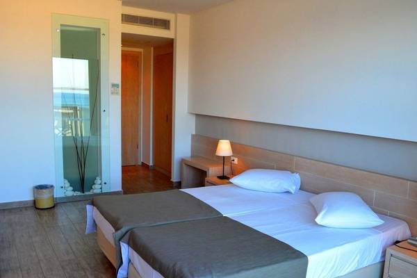 Ein modernes Hotelzimmer im Akti Palace mit zwei Betten, weißen Kissen und einem Nachttisch mit Lampe.