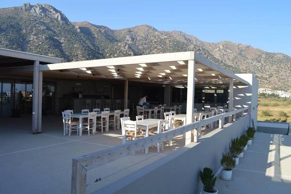 Terrasse des Akti Palace Hotels mit Tischen, Stühlen und Pflanzen vor einem Panorama von Bergen