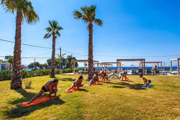 Yoga-Kurs auf der Wiese im Akti Palace Hotel mit Teilnehmern und Palmen im Hintergrund.