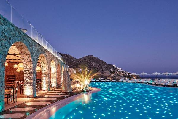 Abendansicht des Pools im Royal Myconian Resort mit beleuchteten Wegen und Sonnenliegen.