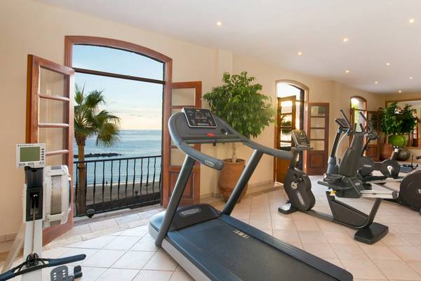 Fitnessraum im Iberostar Grand El Mirador mit Blick auf das Meer und Palmen.