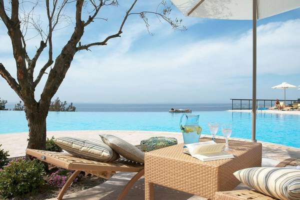 Strandszene mit Liegen und Pool im Ikos Oceania Hotel mit Blick auf das Meer.