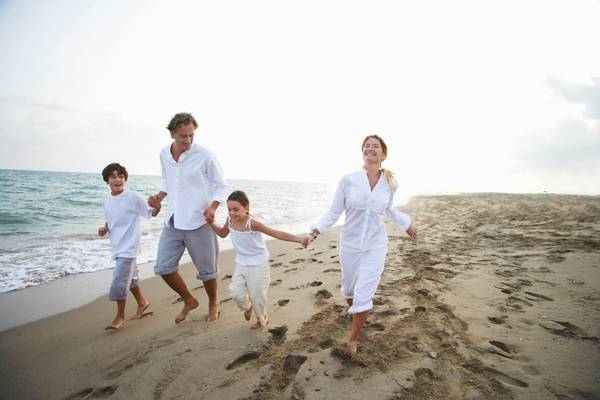 Eine Familie läuft am Strand, alle in weißen Kleidern, mit einem Lächeln auf den Gesichtern.