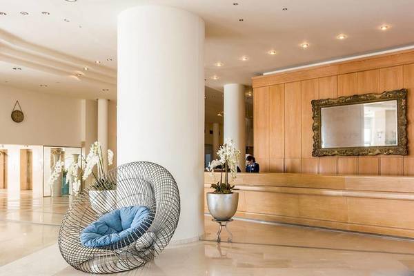 Lobby des Ikos Oceania Hotels mit Rezeption, Holzwänden und Sitzmöbeln.