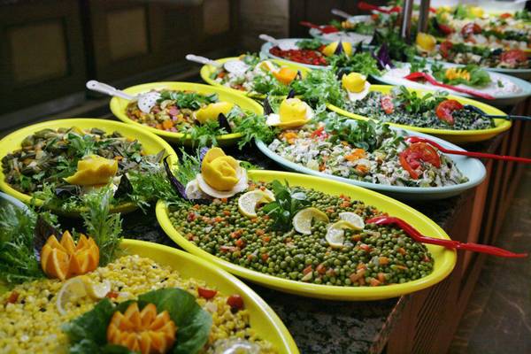 Buffet mit mehreren gelben Platten, gefüllt mit verschiedenen Gemüsesalaten und Beilagen.