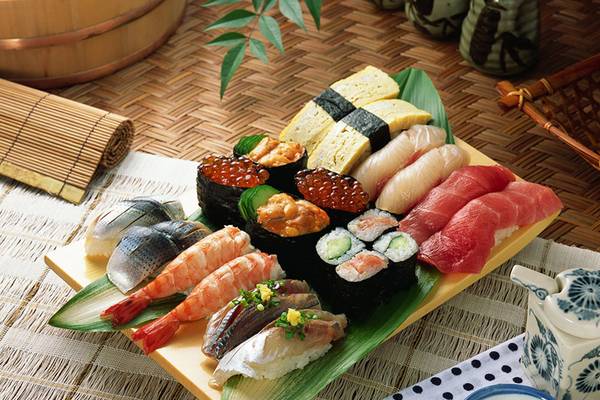 Eine Vielzahl von Sushi auf einem gelben Teller, der auf einem grünen Palmblatt liegt.