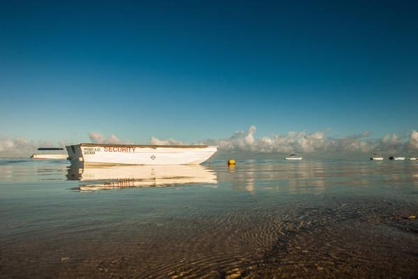 Ein Sicherheitsboot im Wasser am Strand mit Spiegelungen und anderen Booten im Hintergrund.