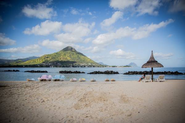 Strand mit Strandhut und Booten im Wasser vor einer Bergkulisse