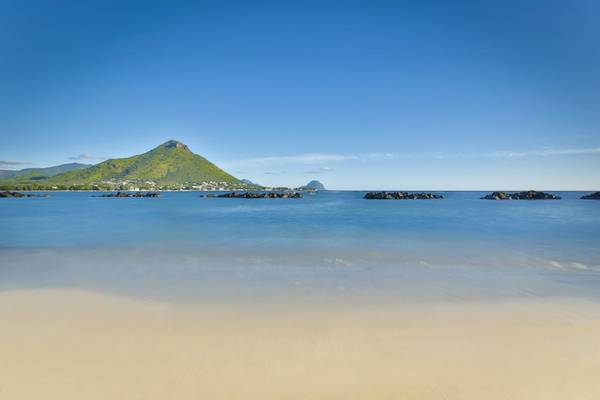 Strand mit Felsen im Wasser und Berg im Hintergrund