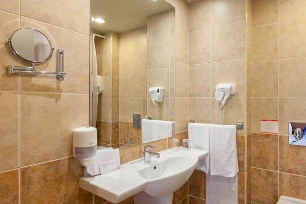 Badezimmer im Sol Luna Bay All Inclusive Hotel mit beigefarbenen Fliesen, einem Waschbecken, Handtüchern und einem Föhn.