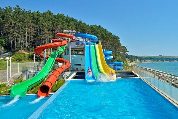 Wasserrutschen am Strand mit Menschen, die hineinspringen, und einer Küste im Hintergrund.
