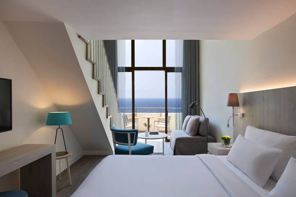 Zimmer im Rhodes Bay Hotel & Spa mit Meerblick, inklusive Bett, Sofa, Tisch und Fenster mit Außenterrasse.