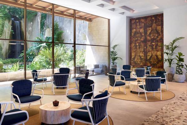 Lounge-Bereich im Rhodes Bay Hotel & Spa mit großen Fenstern, Wasserfall und blauen Stühlen.